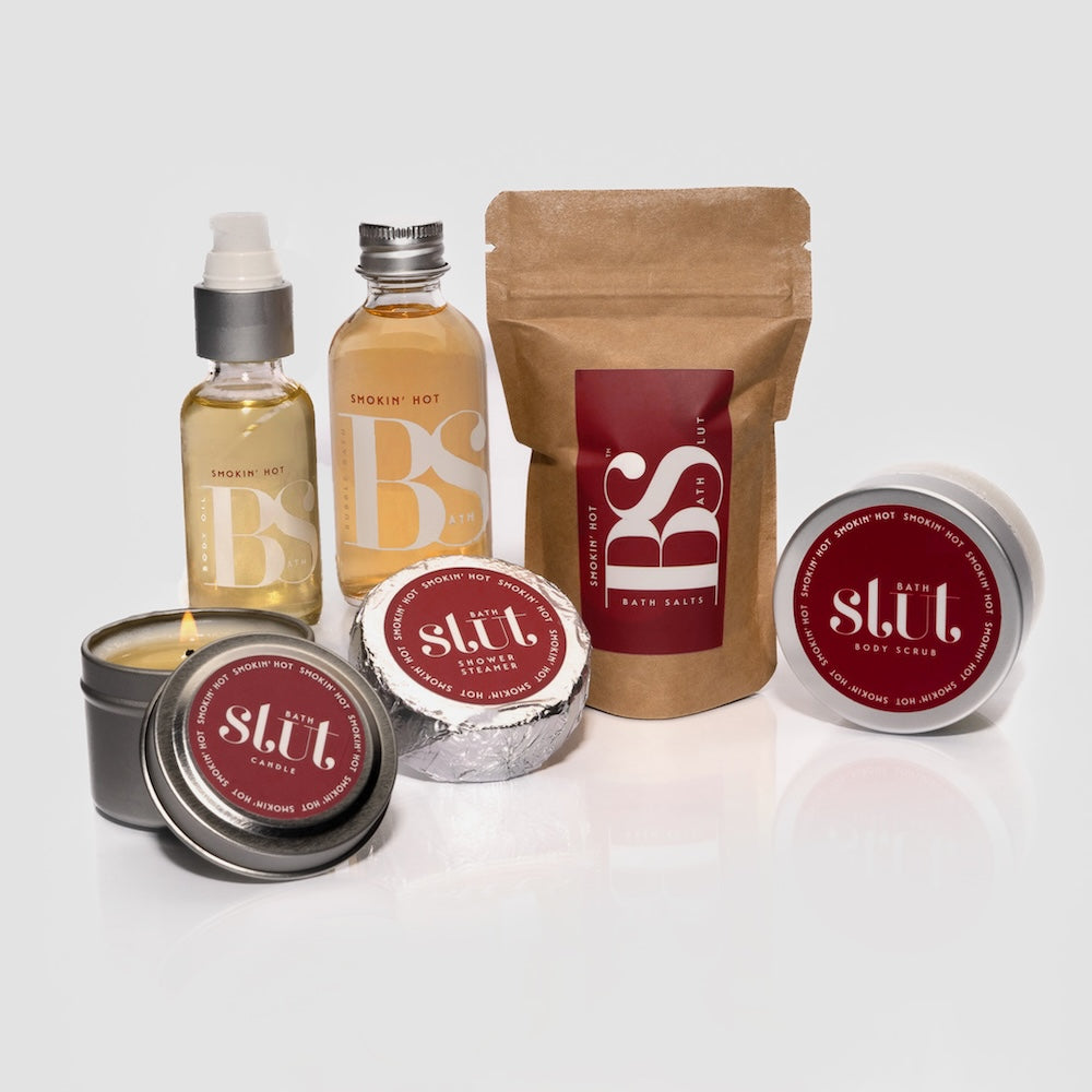 Bath Slut Bath & Body Care Gift Set in Smokin’ Hot scent — travel-size bubble bath, bath salts, body scrub, body oil, shower steamer, and soy candle grouped together.