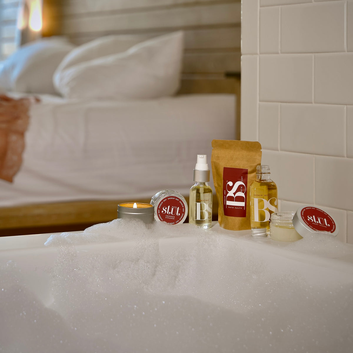 Bath Slut travel-size bath and body gift set in Smokin' Hot, including a bath salts mini pouch, with notes of ginger, jasmine and sandalwood, on the edge of a hotel bathtub