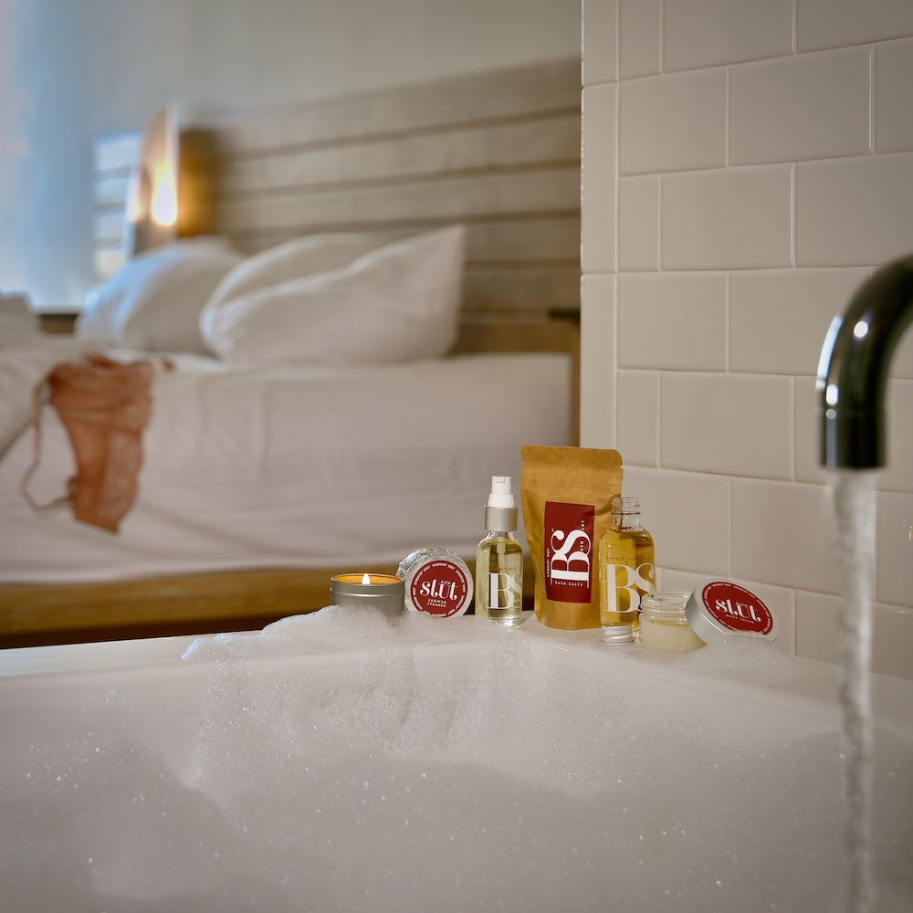 Bath Slut travel-size bath and body gift set in Smokin' Hot, with notes of ginger, jasmine and sandalwood, on the edge of a bathtub in a hotel room