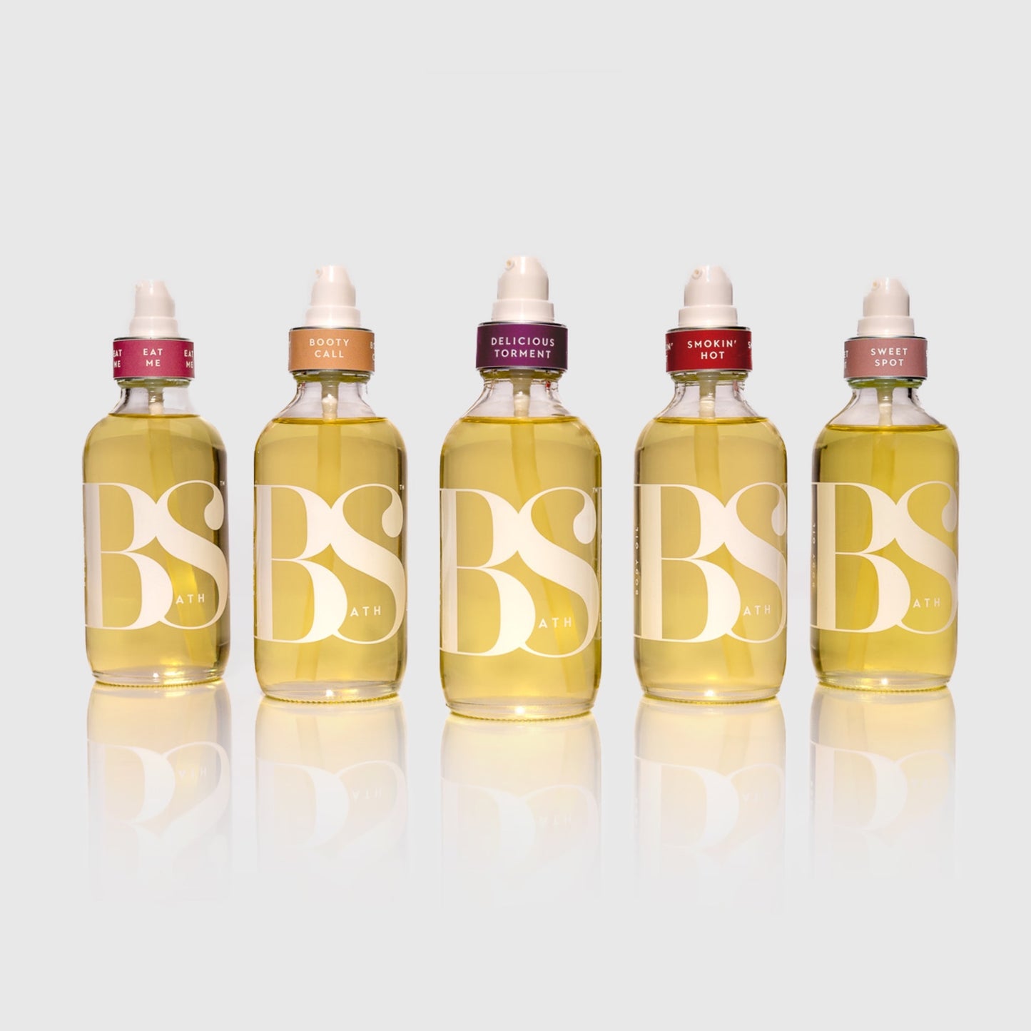 Bath Slut Nourishing Body Oils with Antioxidants in five signature scents — Booty Call, Delicious Torment, Eat Me, Smokin’ Hot, and Sweet Spot — 4 oz glass bottles arranged together.