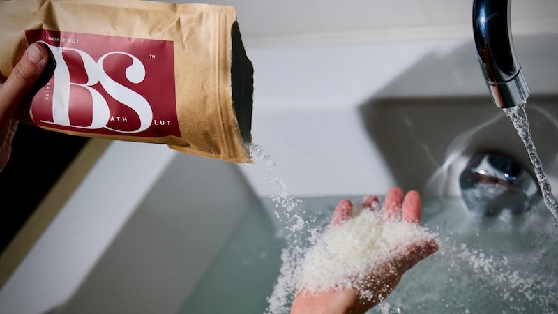 Smokin’ Hot bath salts poured onto a woman’s hand in a bath.